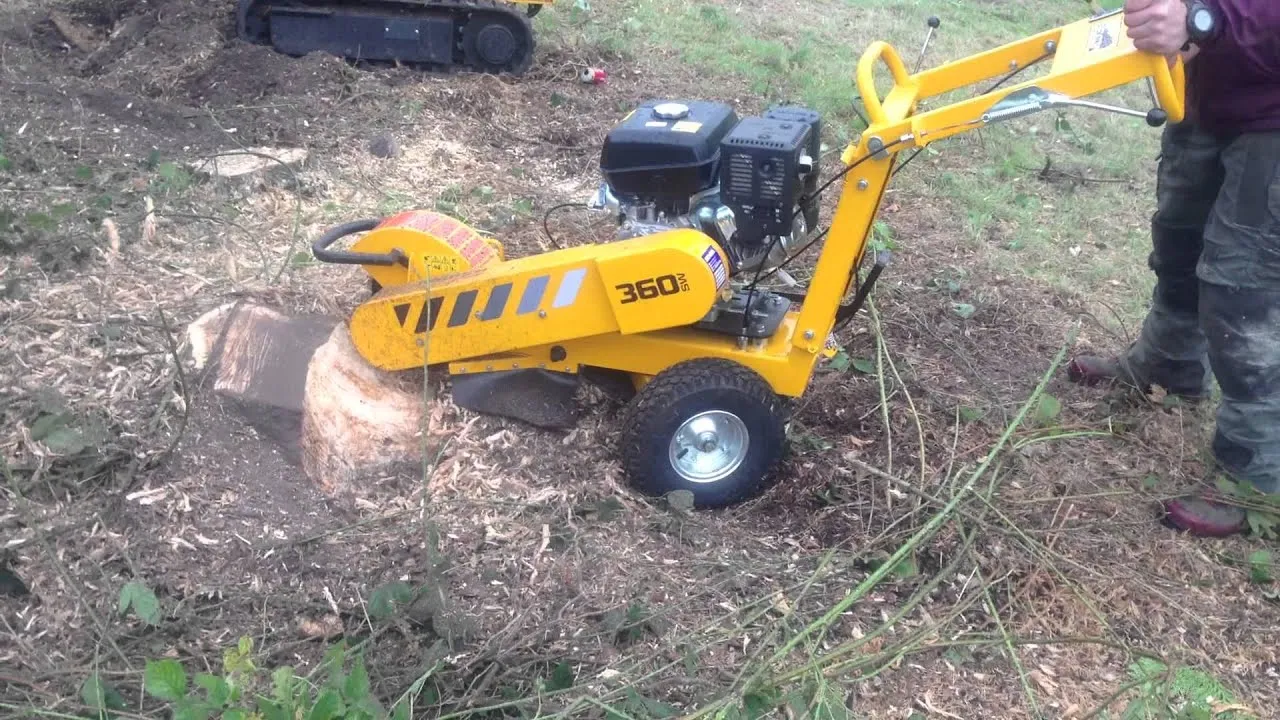 A yellow machine next to a tree stump.