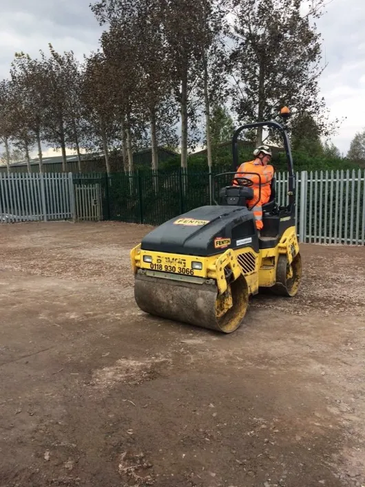A man in an orange jacket is riding a small tractor.